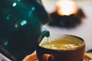 An image of green tea being poured out by a green tea pot into a brown mug